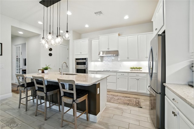 3387 Pilot Cir, Naples, FL 34120 - kitchen featuring appliances with stainless steel finishes, under cabinet range hood, a kitchen island with sink, white cabinetry, and recessed lighting