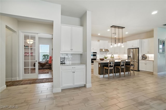 3387 Pilot Cir, Naples, FL 34120 - kitchen featuring stainless steel appliances, a kitchen bar, light countertops, backsplash, and under cabinet range hood