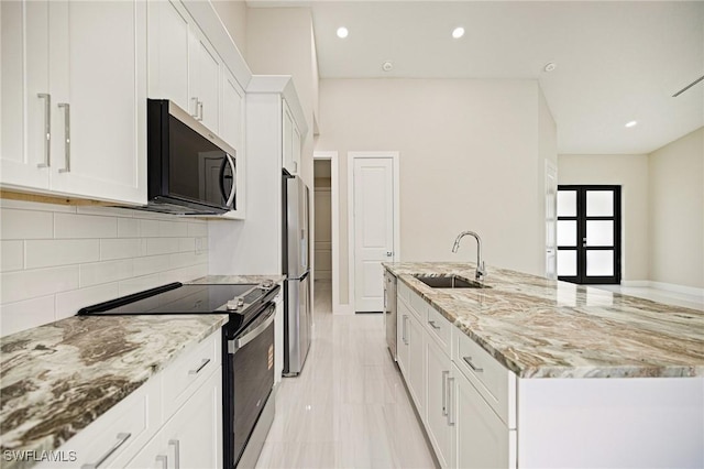 1117 SW Trafalgar Pkwy, Cape Coral, FL 33991 - kitchen with stainless steel appliances, white cabinets, tasteful backsplash, light stone counters, and an island with sink