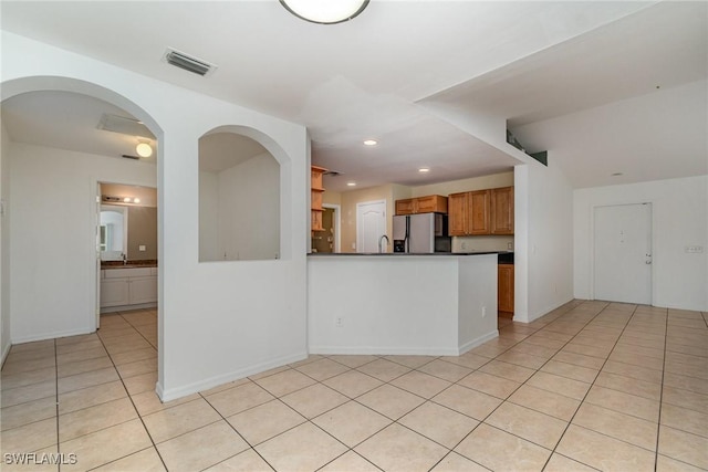 3213 22nd St SW, Lehigh Acres, FL 33976 - kitchen featuring stainless steel fridge with ice dispenser, dark countertops, light tile patterned floors, a peninsula, and brown cabinets