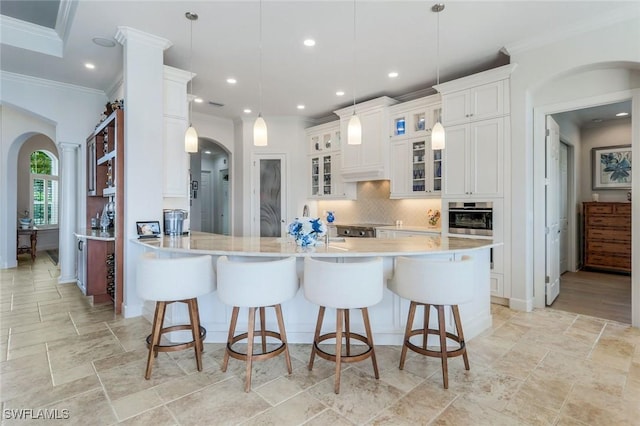 9380 Slate Ct, Naples, FL 34120 - kitchen with arched walkways, crown molding, a kitchen breakfast bar, tasteful backsplash, and white cabinetry