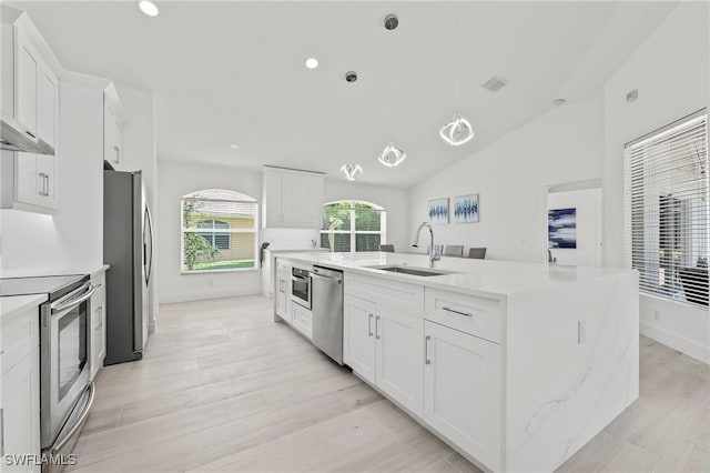 2050 Terrazzo Ln, Naples, FL 34104 - kitchen featuring stainless steel appliances, white cabinets, wall chimney range hood, hanging light fixtures, and light wood-style flooring