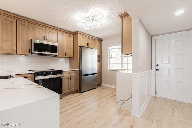 7718 Jewel Ln Unit 101, Naples, FL 34109 - kitchen featuring appliances with stainless steel finishes, light wood finished floors, brown cabinetry, backsplash, and light stone counters