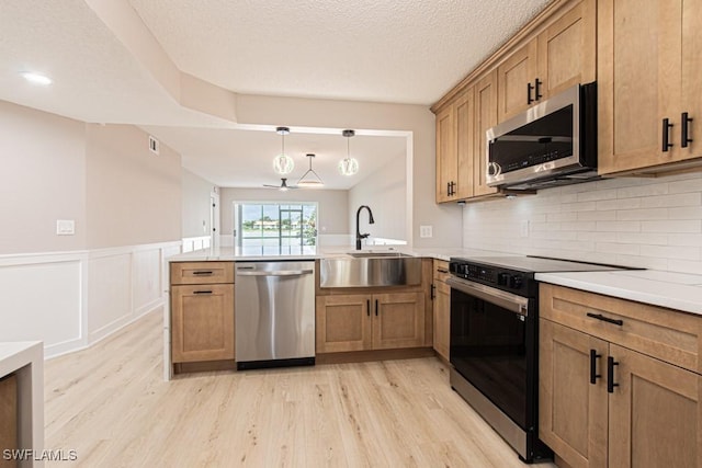 7718 Jewel Ln Unit 101, Naples, FL 34109 - kitchen with stainless steel appliances, a peninsula, light wood-style flooring, decorative backsplash, and wainscoting