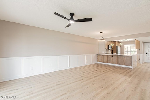7718 Jewel Ln Unit 101, Naples, FL 34109 - unfurnished living room with light wood finished floors, a ceiling fan, wainscoting, a decorative wall, and a textured ceiling
