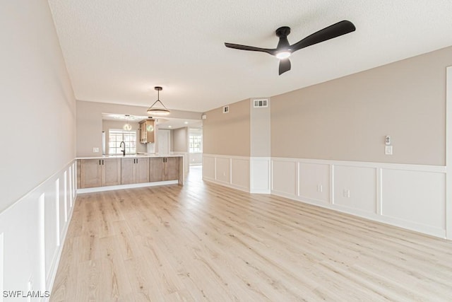7718 Jewel Ln Unit 101, Naples, FL 34109 - unfurnished living room with a decorative wall, light wood-style floors, a textured ceiling, ceiling fan, and wainscoting