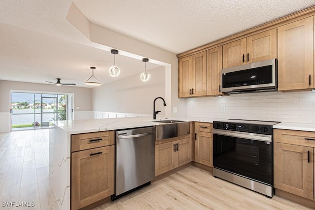 7718 Jewel Ln Unit 101, Naples, FL 34109 - kitchen with appliances with stainless steel finishes, a peninsula, light wood finished floors, decorative backsplash, and pendant lighting