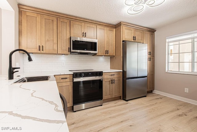 7718 Jewel Ln Unit 101, Naples, FL 34109 - kitchen featuring appliances with stainless steel finishes, decorative backsplash, light wood-style flooring, light stone counters, and a textured ceiling