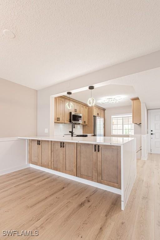 7718 Jewel Ln Unit 101, Naples, FL 34109 - kitchen featuring stainless steel microwave, light wood-style flooring, freestanding refrigerator, a textured ceiling, and light countertops