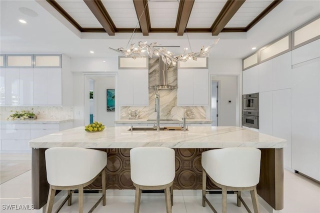 309 Neapolitan Way, Naples, FL 34103 - kitchen with stainless steel oven, modern cabinets, decorative backsplash, wall chimney range hood, and a kitchen breakfast bar