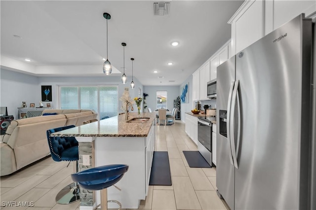 1421 SW 13th Ter, Cape Coral, FL 33991 - kitchen with stainless steel appliances, a breakfast bar, white cabinetry, dark stone counters, and a kitchen island with sink