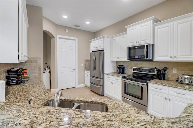 14642 Speranza Way, Bonita Springs, FL 34135 - kitchen featuring stainless steel appliances, light stone countertops, white cabinets, decorative backsplash, and arched walkways