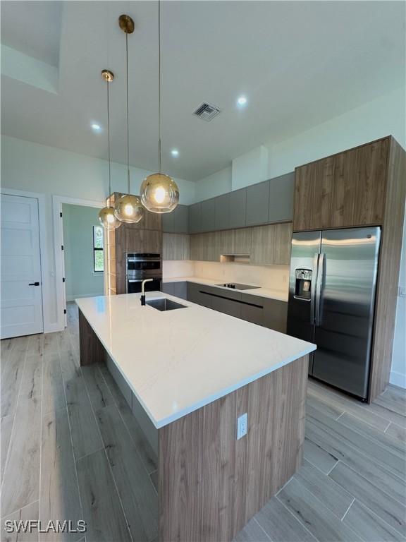 2660 18th Ave NE, Naples, FL 34120 - kitchen with stainless steel fridge, modern cabinets, light wood-type flooring, a spacious island, and light countertops