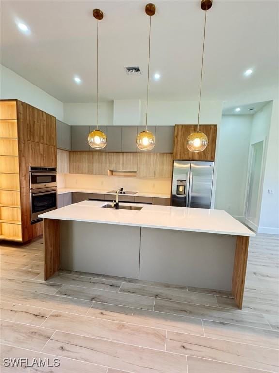 2660 18th Ave NE, Naples, FL 34120 - kitchen featuring appliances with stainless steel finishes, light wood-style floors, a large island with sink, modern cabinets, and light countertops