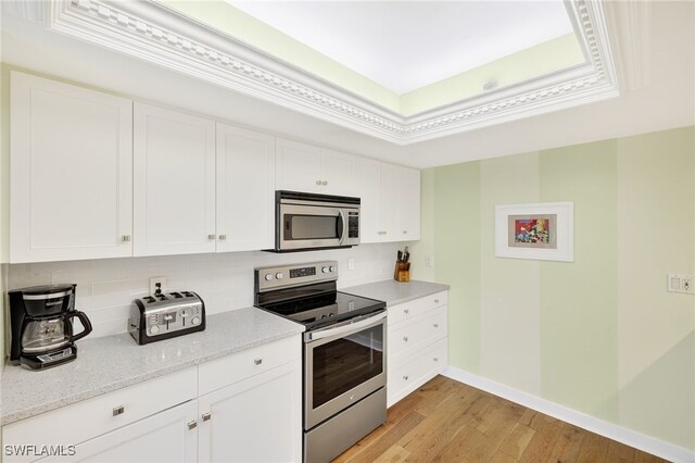 33 Urchin Ct, Captiva, FL 33924 - kitchen with stainless steel appliances, backsplash, light wood-type flooring, white cabinetry, and a raised ceiling