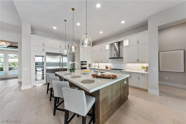 8923 Nevis Way, Naples, FL 34112 - kitchen featuring wall chimney exhaust hood, stainless steel appliances, a large island with sink, tasteful backsplash, and light countertops