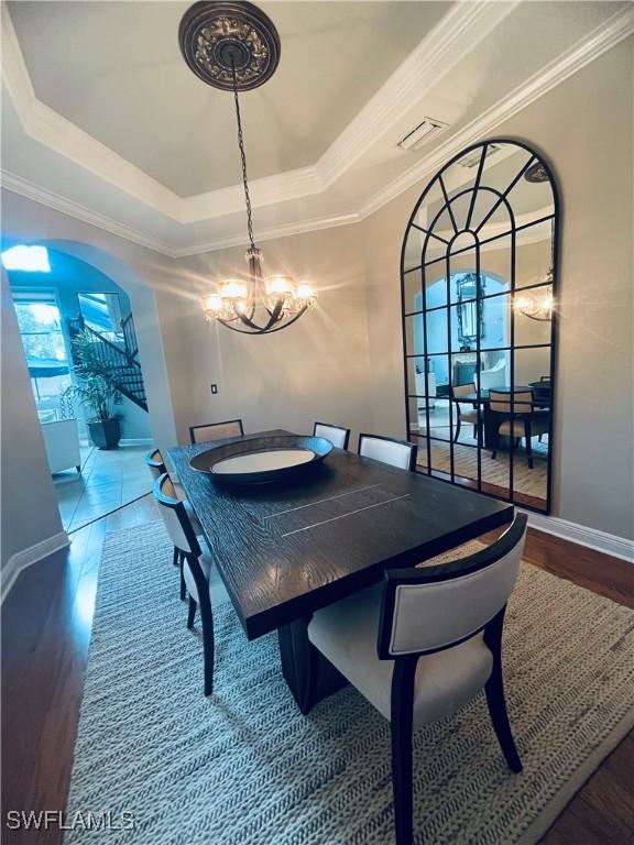 23056 Sanabria Loop, Bonita Springs, FL 34135 - dining room featuring a tray ceiling, a chandelier, wood finished floors, ornamental molding, and arched walkways