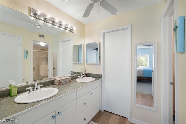 1086 Forest Lakes Dr Unit 9106, Naples, FL 34105 - bathroom featuring a ceiling fan, double vanity, a shower with door, wood finished floors, and a textured ceiling