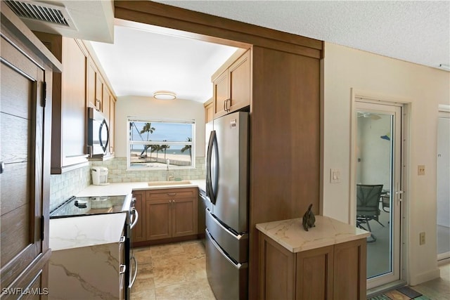 25710 Hickory Blvd Unit A 202, Bonita Springs, FL 34134 - kitchen with stainless steel appliances, light stone counters, decorative backsplash, and brown cabinets