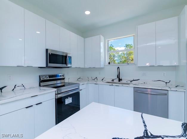 3103 13th St SW, Lehigh Acres, FL 33976 - kitchen with appliances with stainless steel finishes, modern cabinets, white cabinets, light stone countertops, and recessed lighting