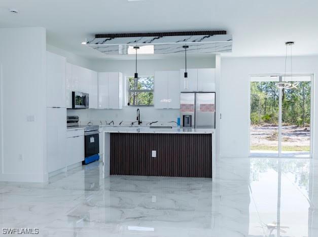 3103 13th St SW, Lehigh Acres, FL 33976 - kitchen featuring stainless steel appliances, white cabinets, hanging light fixtures, a center island, and light countertops