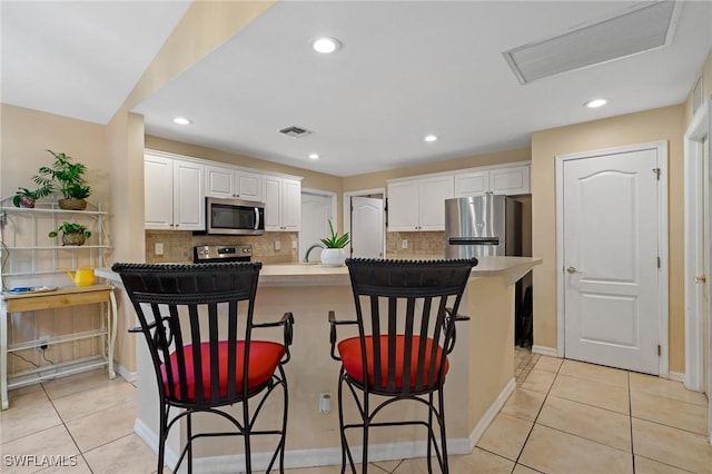 873 Spaulding St E, Lehigh Acres, FL 33974 - kitchen featuring appliances with stainless steel finishes, white cabinets, backsplash, light tile patterned flooring, and a kitchen bar