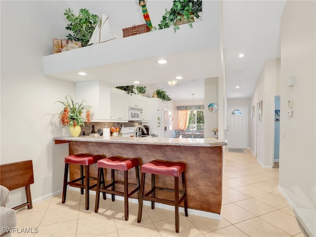 6790 Beach Resort Dr Unit 14, Naples, FL 34114 - kitchen featuring white appliances, a peninsula, white cabinetry, a breakfast bar, and recessed lighting