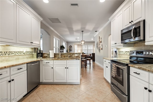 12977 Turtle Cove Trl, North Fort Myers, FL 33903 - kitchen with stainless steel appliances, ornamental molding, a peninsula, arched walkways, and white cabinetry