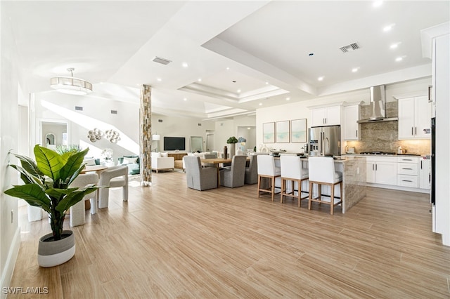 5203 Starfish Ave, Naples, FL 34103 - kitchen featuring stainless steel refrigerator with ice dispenser, wall chimney exhaust hood, backsplash, a kitchen bar, and an island with sink