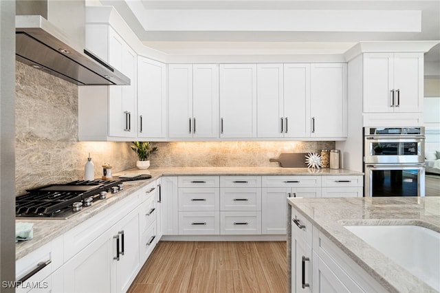 5203 Starfish Ave, Naples, FL 34103 - kitchen with wall chimney exhaust hood, stainless steel appliances, white cabinets, and backsplash