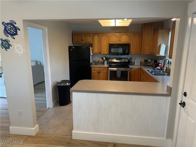 120 Bay Mar Dr, Fort Myers Beach, FL 33931 - kitchen with black appliances, a peninsula, brown cabinets, light countertops, and light wood-style floors