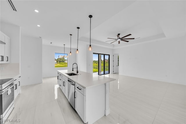 542 Raintree St E, Lehigh Acres, FL 33974 - kitchen featuring appliances with stainless steel finishes, ceiling fan, a tray ceiling, a center island with sink, and white cabinetry