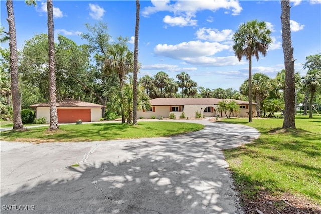 18381 Panther Trail Ln, North Fort Myers, FL 33917 - ranch-style house featuring a front yard, stucco siding, driveway, a detached garage, and view of wooded area