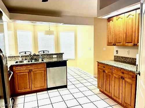 4619 SW 20th Pl, Cape Coral, FL 33914 - kitchen featuring stainless steel dishwasher, light tile patterned floors, brown cabinetry, and stone countertops