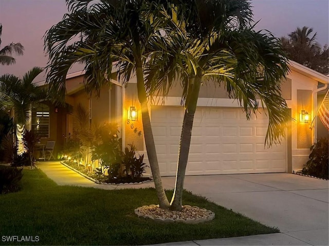 8644 Ibis Cove Cir, Naples, FL 34119 - property exterior at dusk featuring driveway, a garage, stucco siding, and a yard