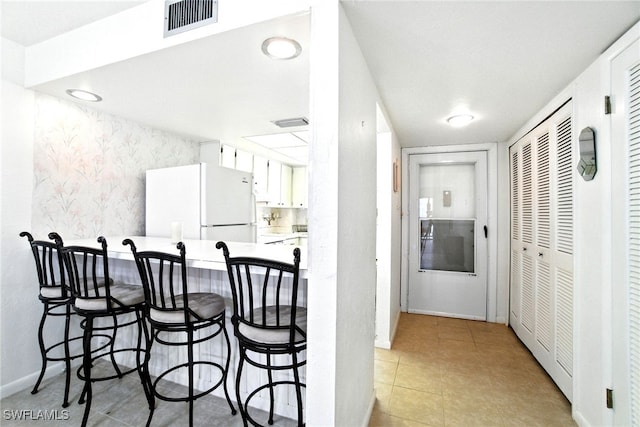 2079 Barkeley Ln Unit 6, Fort Myers, FL 33907 - kitchen with wallpapered walls, freestanding refrigerator, white cabinetry, a breakfast bar, and an accent wall