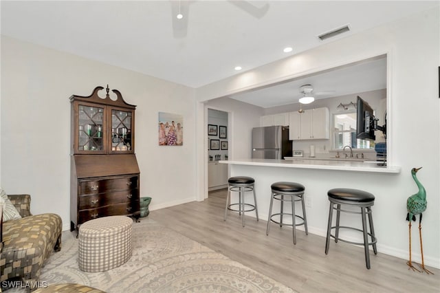 1308 Hull St S, Gulfport, FL 33707 - kitchen with freestanding refrigerator, a ceiling fan, a breakfast bar area, white cabinets, and light wood-type flooring