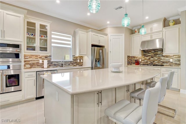 8142 Lucello Ter S, Naples, FL 34114 - kitchen featuring appliances with stainless steel finishes, under cabinet range hood, a center island, backsplash, and crown molding