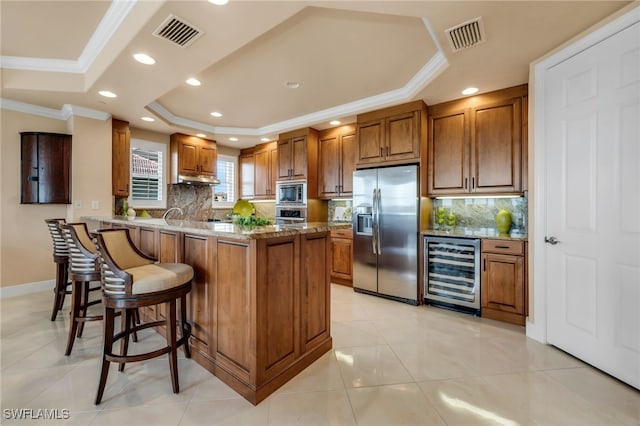 580 El Camino Real Unit 3606, Naples, FL 34119 - kitchen with stainless steel appliances, wine cooler, a tray ceiling, brown cabinets, and ornamental molding