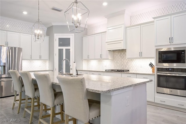 2110 Antigua Ln, Naples, FL 34120 - kitchen featuring appliances with stainless steel finishes, crown molding, a chandelier, decorative backsplash, and a center island with sink
