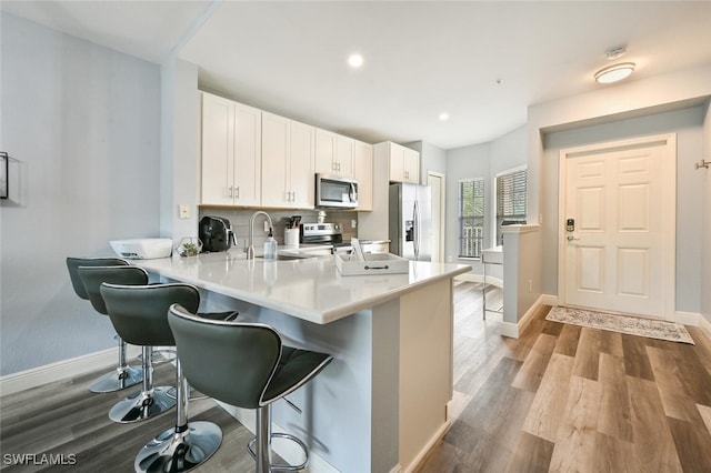 9175 Celeste Dr Unit 305, Naples, FL 34113 - kitchen featuring stainless steel appliances, a breakfast bar, wood finished floors, light countertops, and white cabinetry