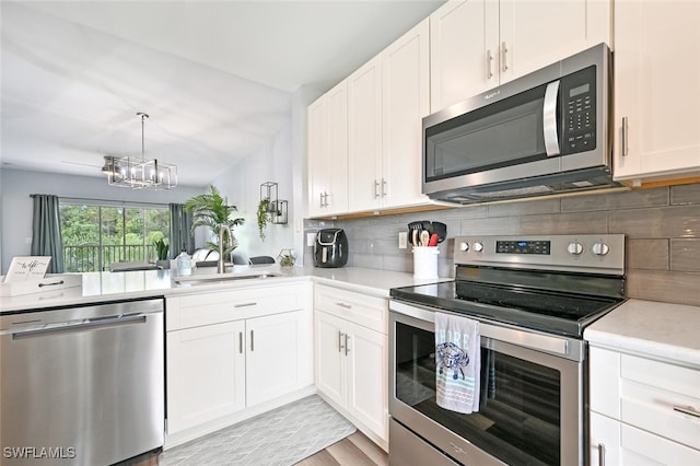 9175 Celeste Dr Unit 305, Naples, FL 34113 - kitchen featuring appliances with stainless steel finishes, a chandelier, decorative backsplash, white cabinets, and light wood-style floors