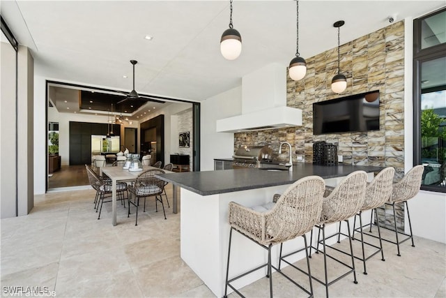 10411 Via Parma Way, Miromar Lakes, FL 33913 - kitchen featuring dark countertops, premium range hood, a raised ceiling, light tile patterned flooring, and a kitchen bar