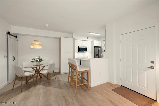 1170 Reserve Way Unit 107, Naples, FL 34105 - kitchen with appliances with stainless steel finishes, white cabinetry, a breakfast bar area, light wood-type flooring, and a barn door