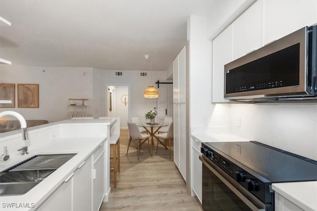 1170 Reserve Way Unit 107, Naples, FL 34105 - kitchen featuring electric range, stainless steel microwave, light wood-style floors, white cabinets, and light countertops