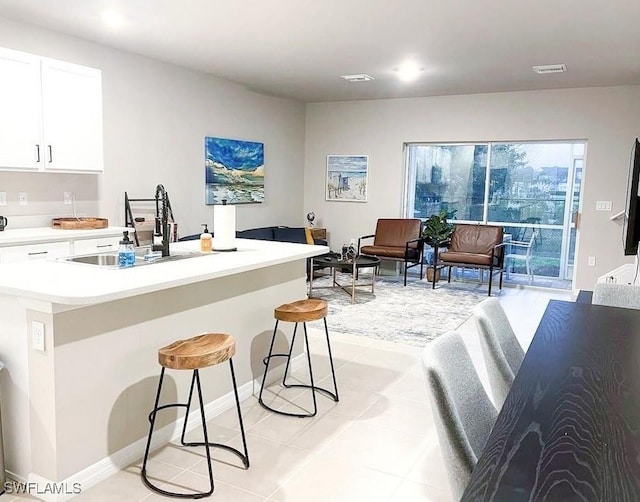 15141 Wildflower Cir, Naples, FL 34119 - kitchen with light countertops, light tile patterned flooring, a breakfast bar, white cabinets, and a kitchen island with sink