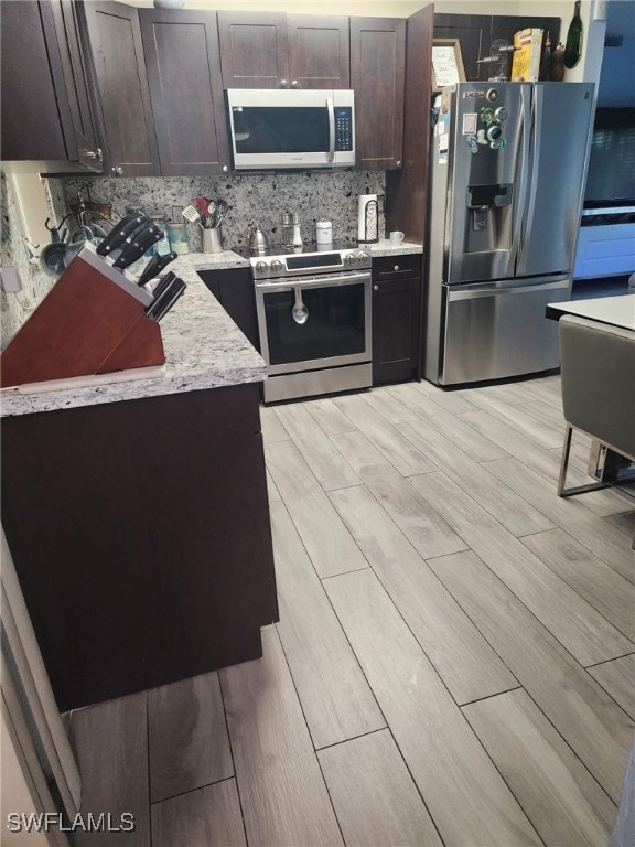 3101 12th St W, Lehigh Acres, FL 33971 - kitchen with stainless steel appliances, wood tiled floors, dark brown cabinetry, tasteful backsplash, and light stone counters