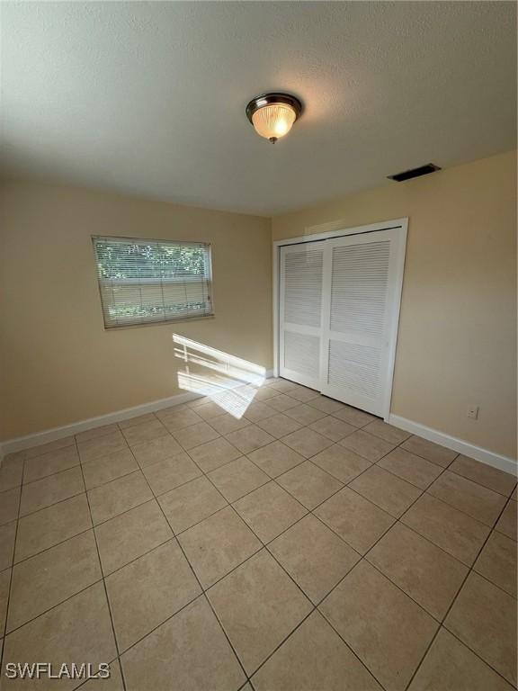 401 W Oregon Rd, Lehigh Acres, FL 33971 - unfurnished bedroom with tile patterned flooring, a closet, and a textured ceiling