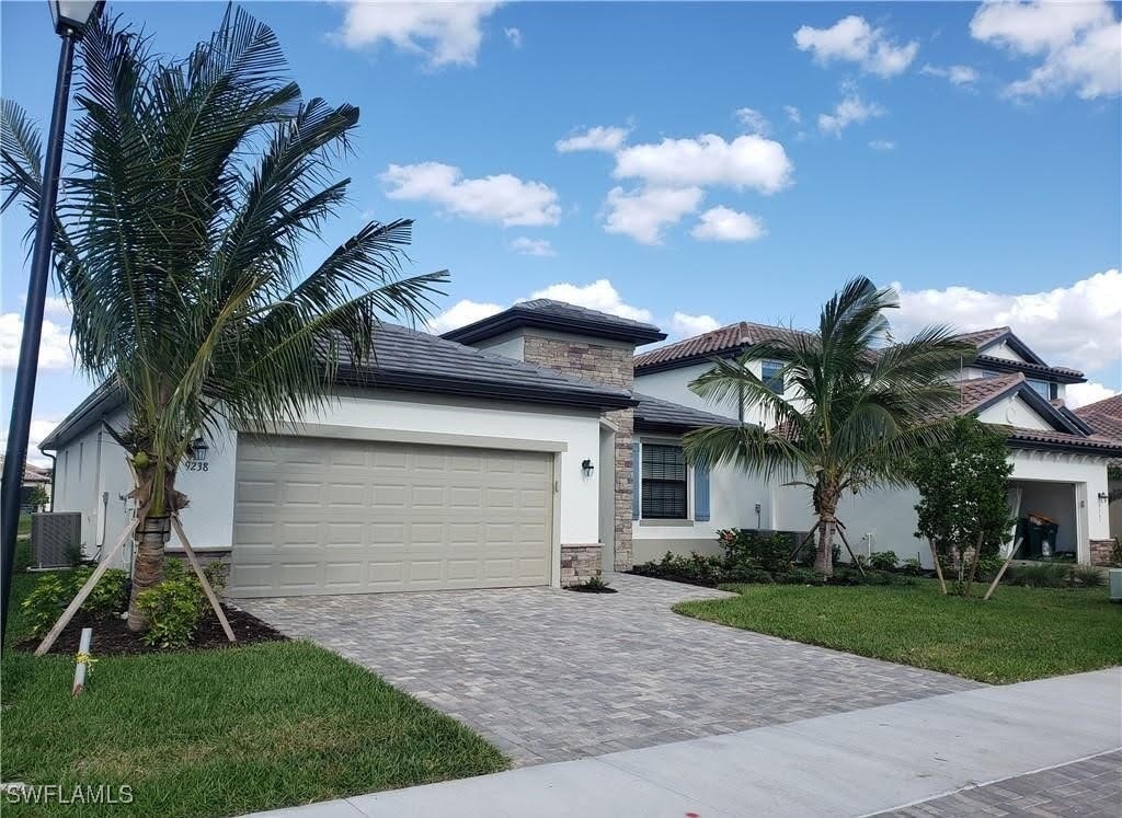9238 Shadow Oak Ln, Naples, FL 34120 - view of front of home featuring stucco siding, an attached garage, decorative driveway, and stone siding