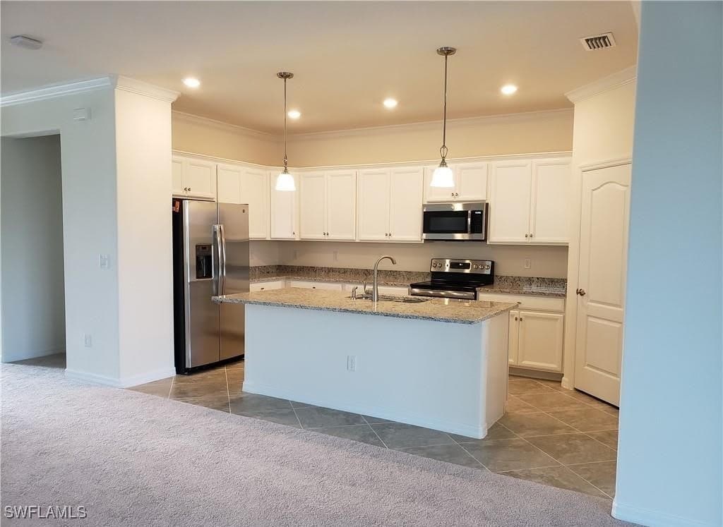 9238 Shadow Oak Ln, Naples, FL 34120 - kitchen with stainless steel appliances, ornamental molding, white cabinetry, light stone counters, and an island with sink